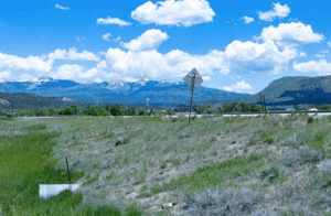 Mountainous landscape with grasslands near commercial property for sale in Colorado, with snowy peaks and clouds.
